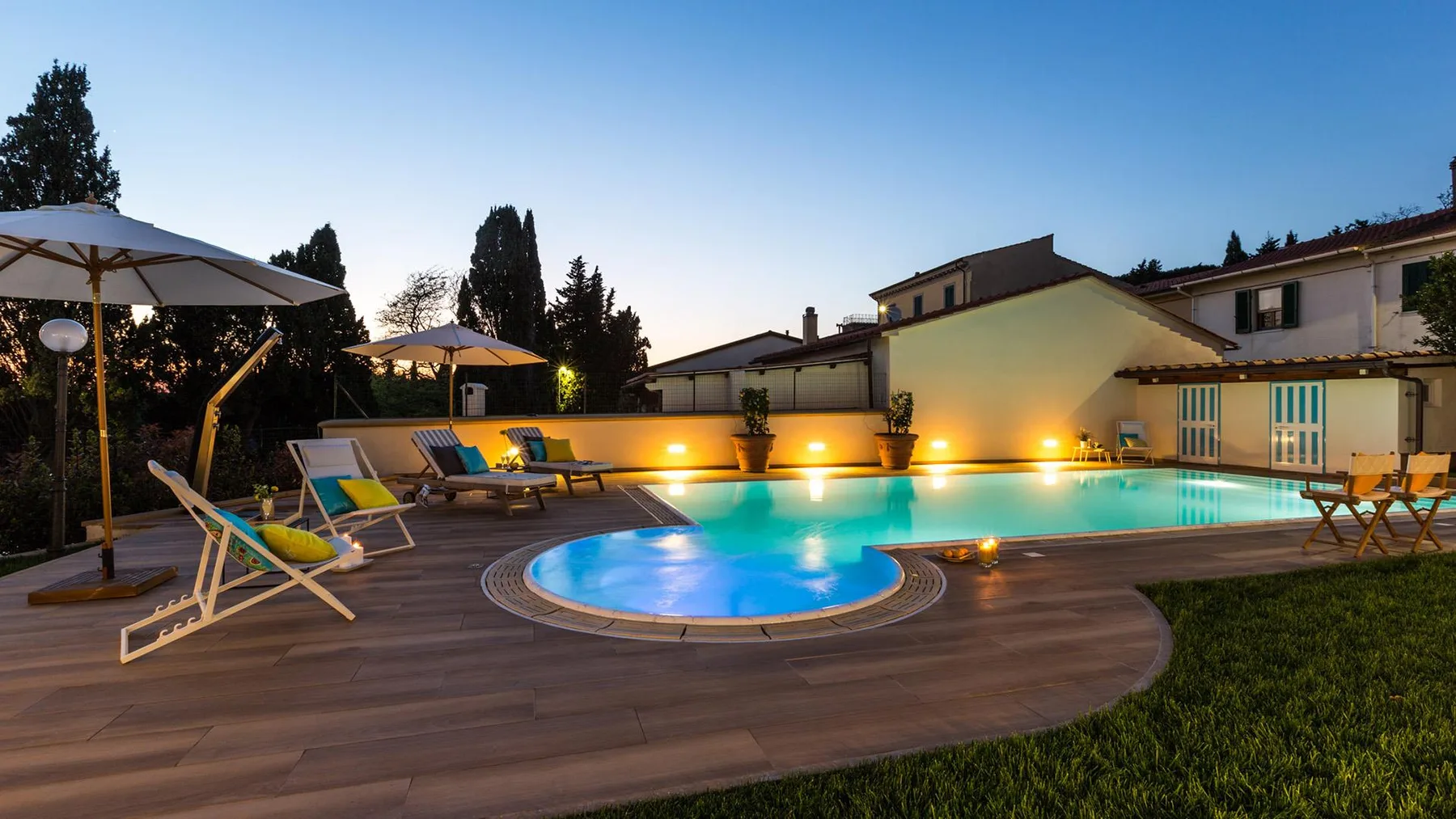 An outdoor swimming pool and circular spa sit beside a wooden deck and lounge seating.