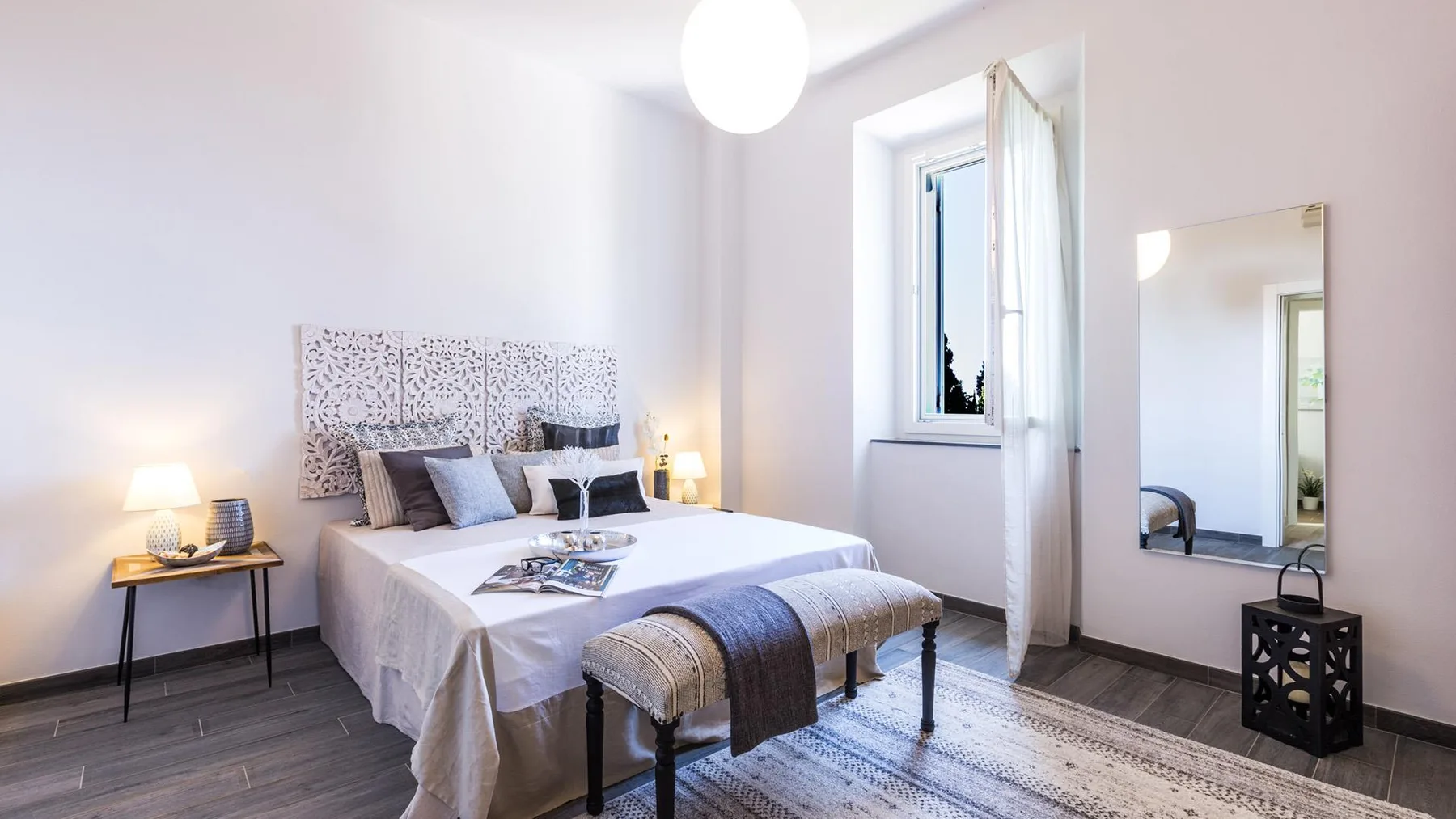 A bright bedroom with a neatly made bed and a window beside it.