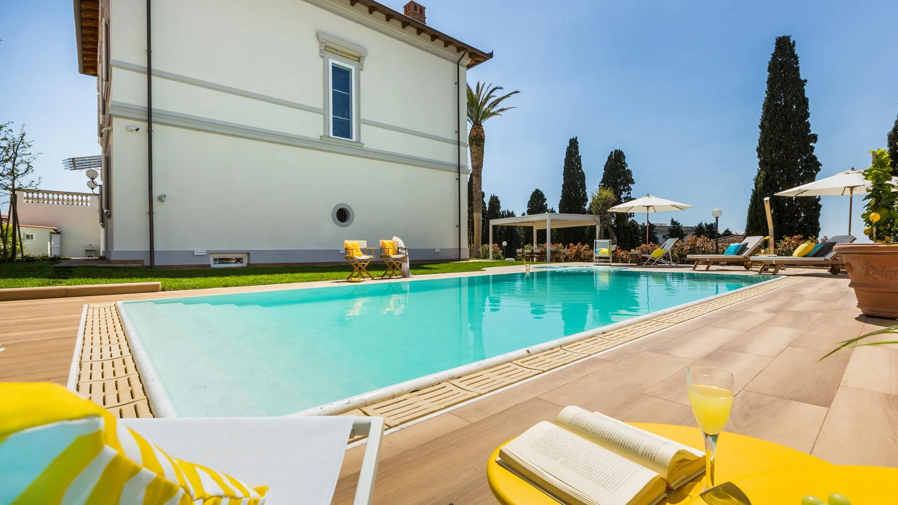 An outdoor swimming pool beside a white building, with lounge seating on the surrounding deck.