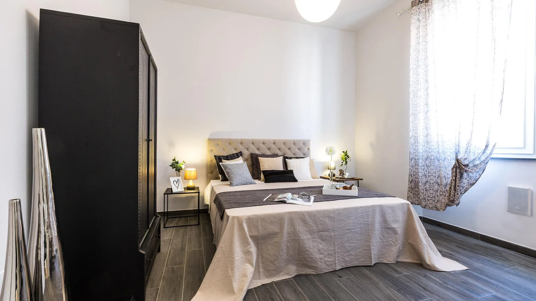A bedroom with a neatly made bed, bedside tables, and a tall dark wardrobe.