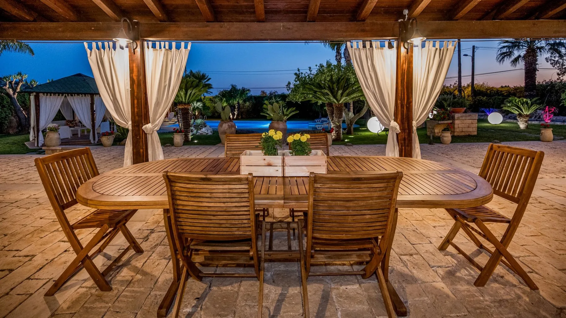 Una zona de comedor exterior cubierta da a un jardín con piscina.