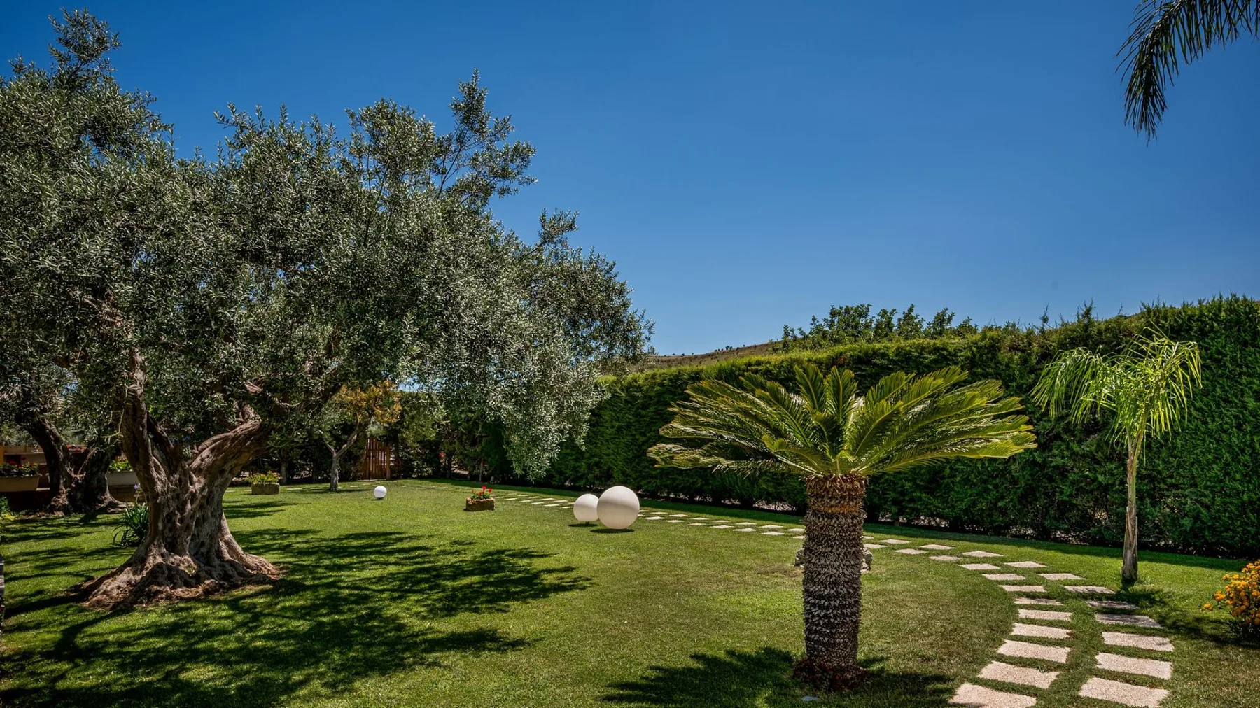 Un jardín ajardinado con césped, árboles frondosos y un sendero de piedra.