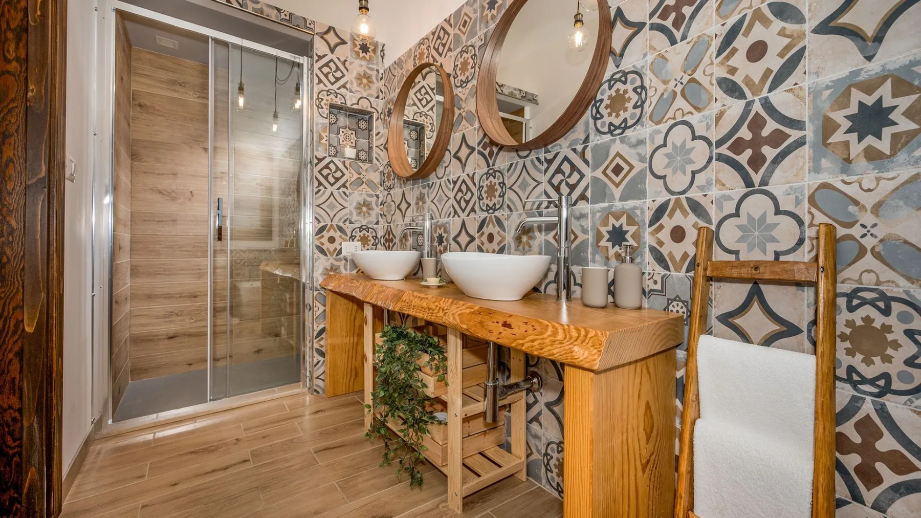 Un baño con azulejos estampados, un mueble de madera y una ducha de vidrio.