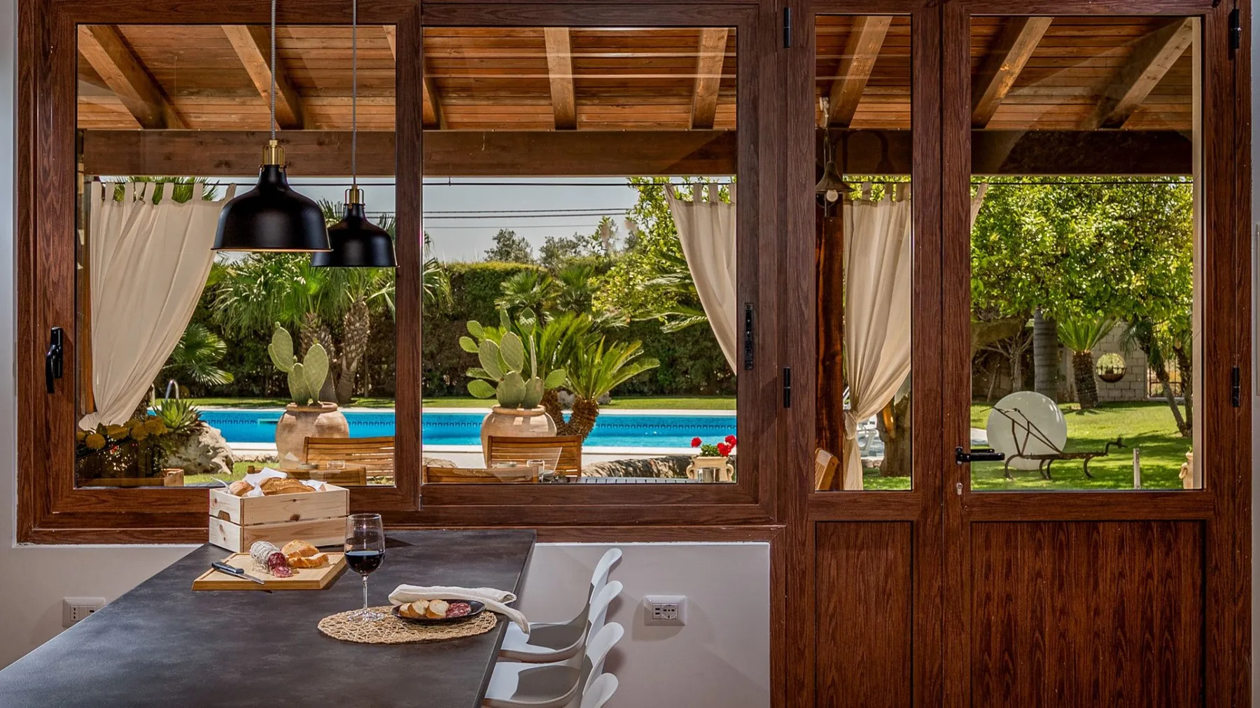 Un comedor da a una piscina y un jardín a través de grandes ventanas de madera.