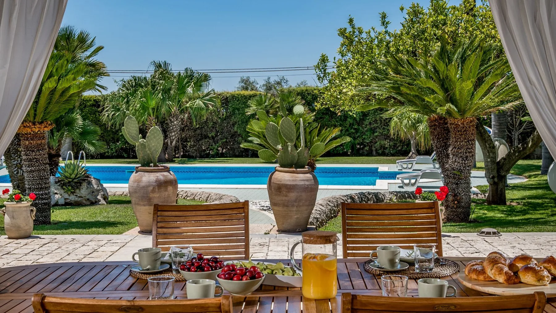 Una mesa de comedor en la terraza del jardín da a una piscina y abundante vegetación.