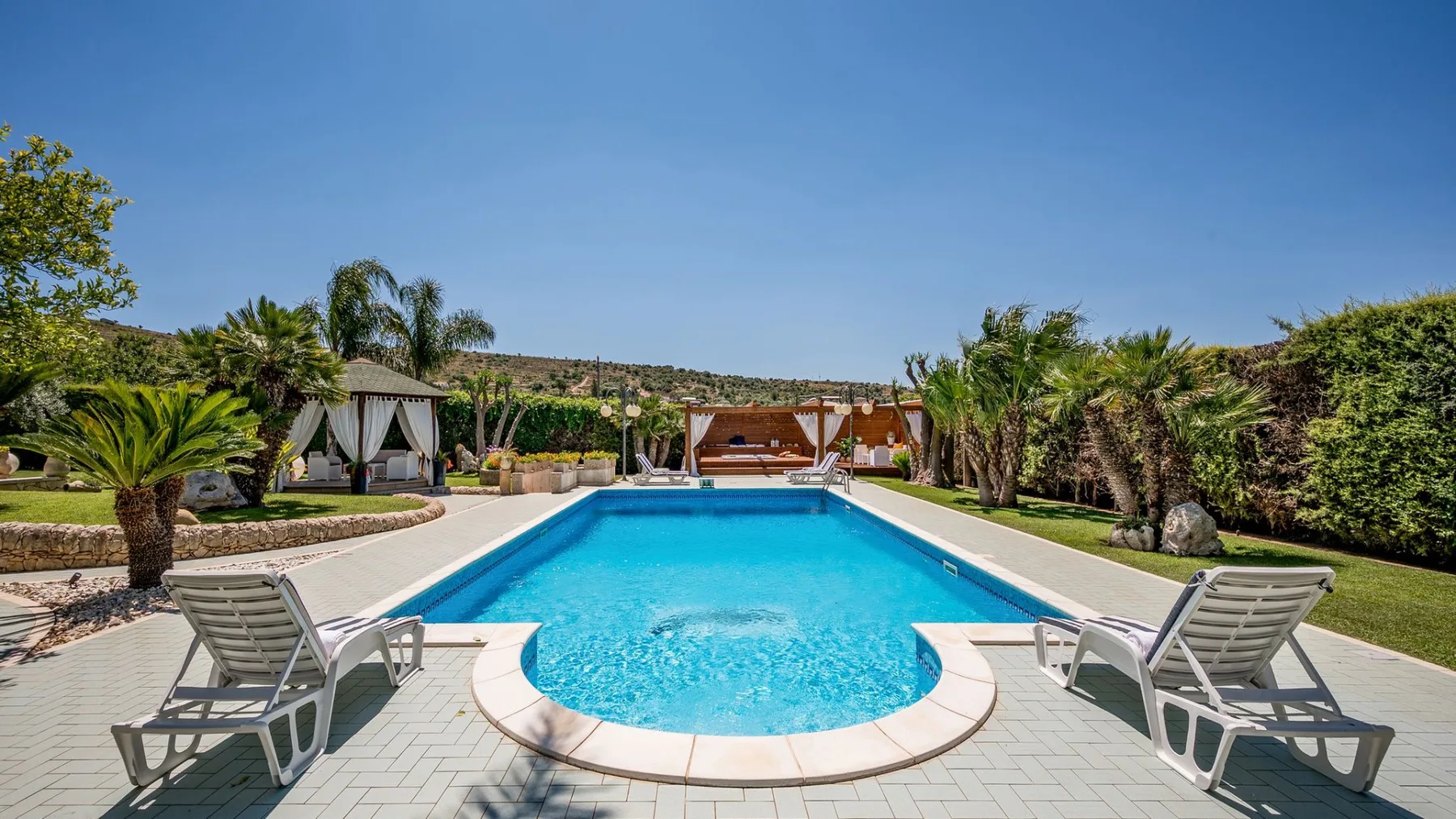 Una piscina está en un patio exterior ajardinado con asientos para descansar.