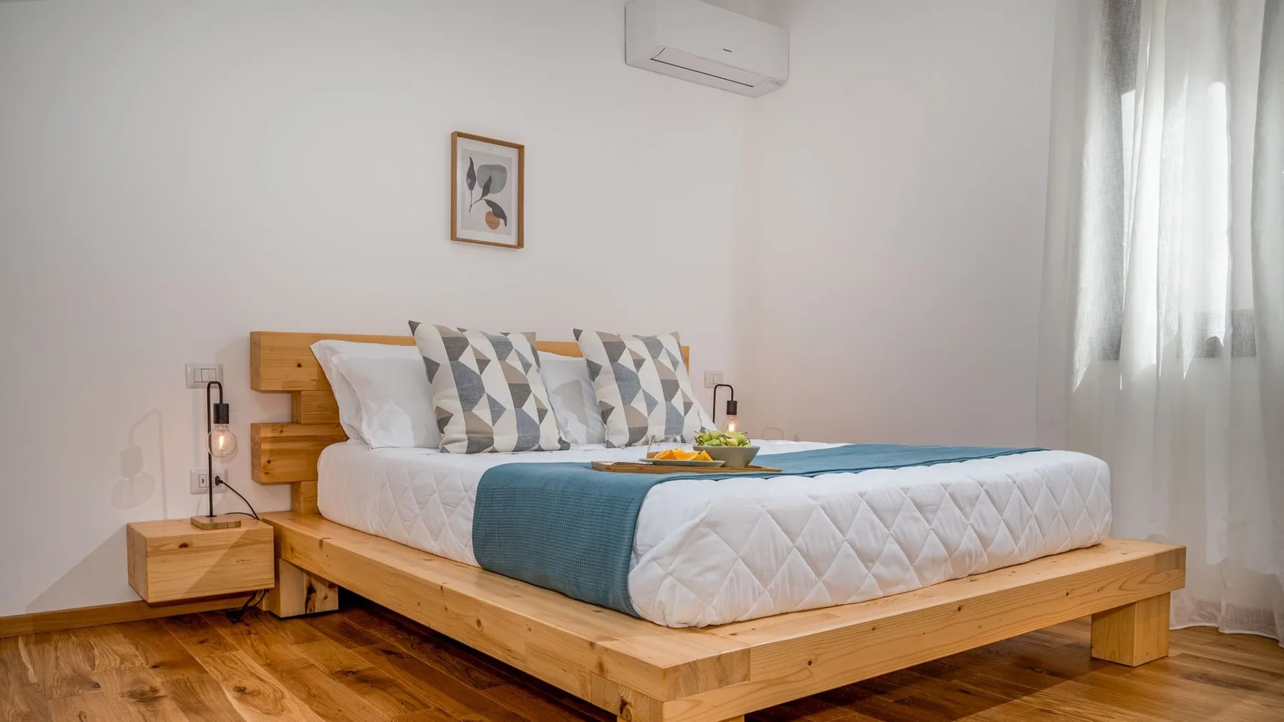 Un dormitorio con una cama de madera, almohadas estampadas y un camino de cama verde azulado.