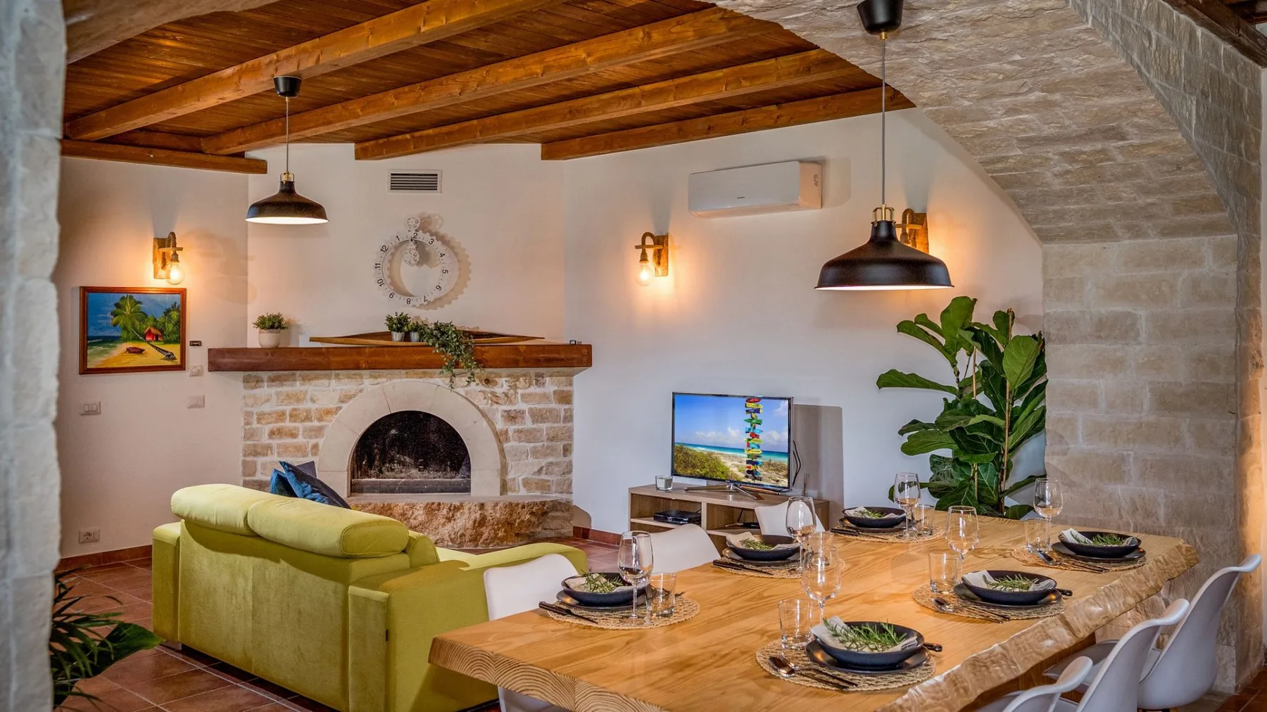 Un comedor y sala de estar con una mesa de madera, asientos verdes y una chimenea de piedra.
