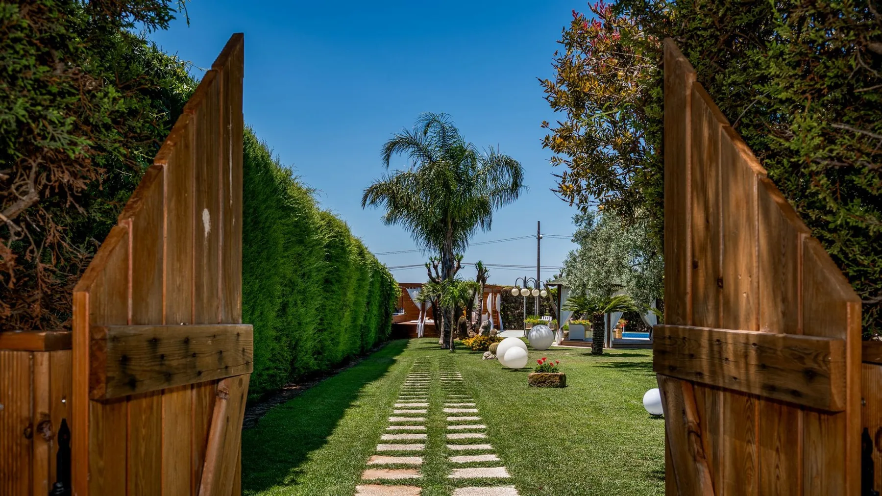 Una puerta de madera abierta da a un jardín con césped y un camino de piedras.
