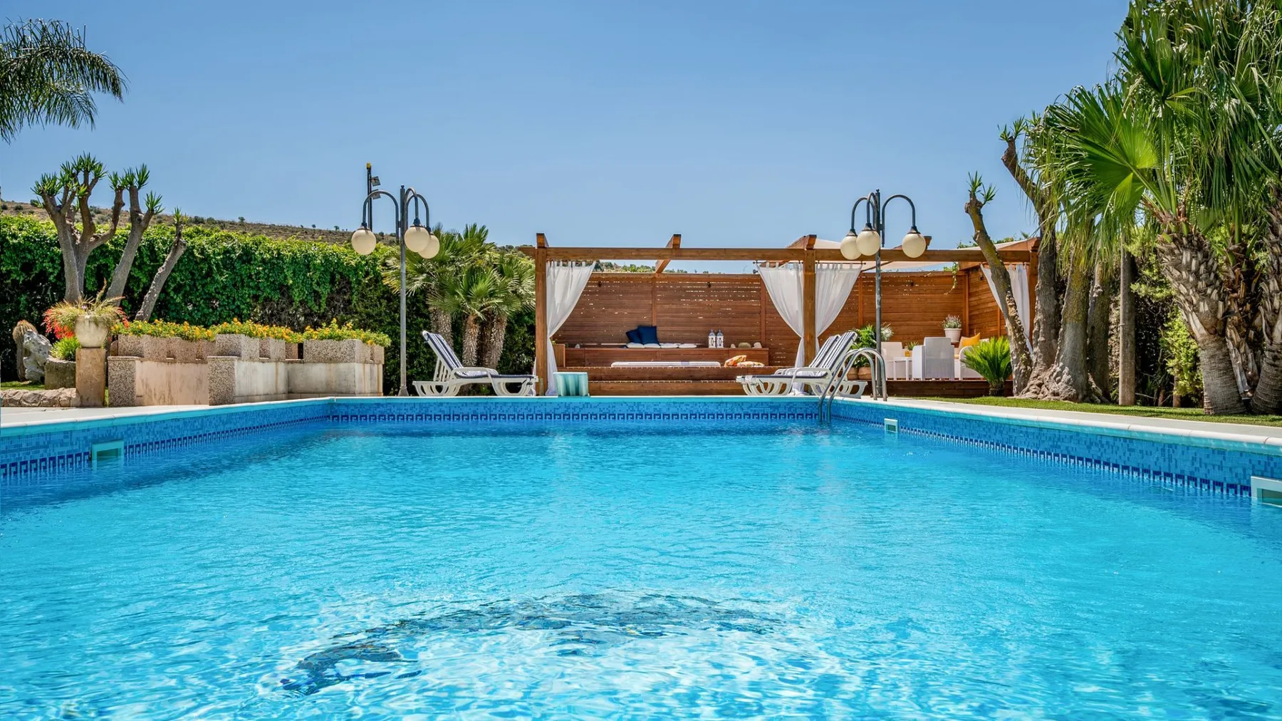 Una piscina al aire libre con una zona de descanso a la sombra y palmeras.