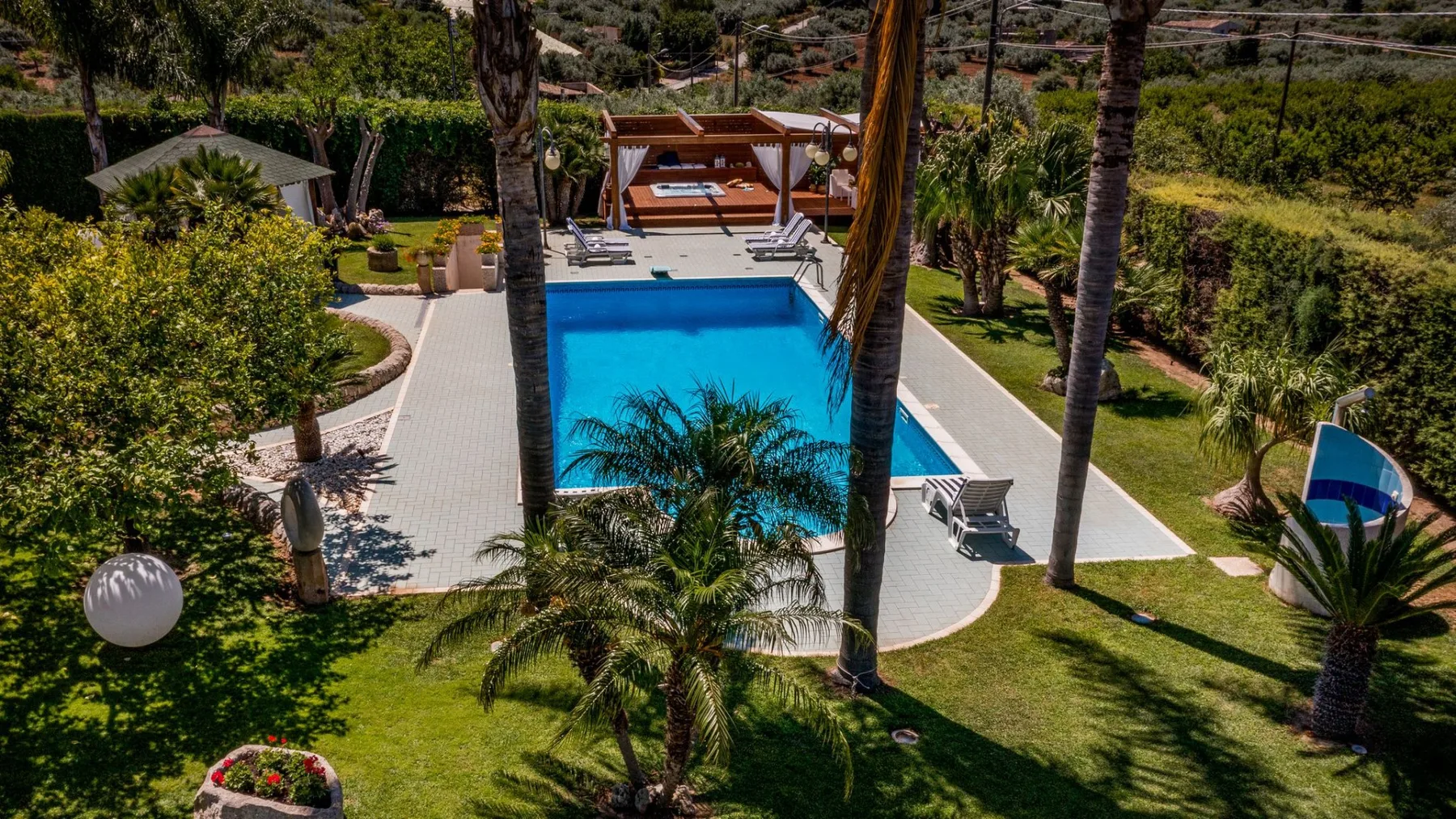 Una zona de piscina al aire libre ajardinada, con césped y palmeras alrededor.