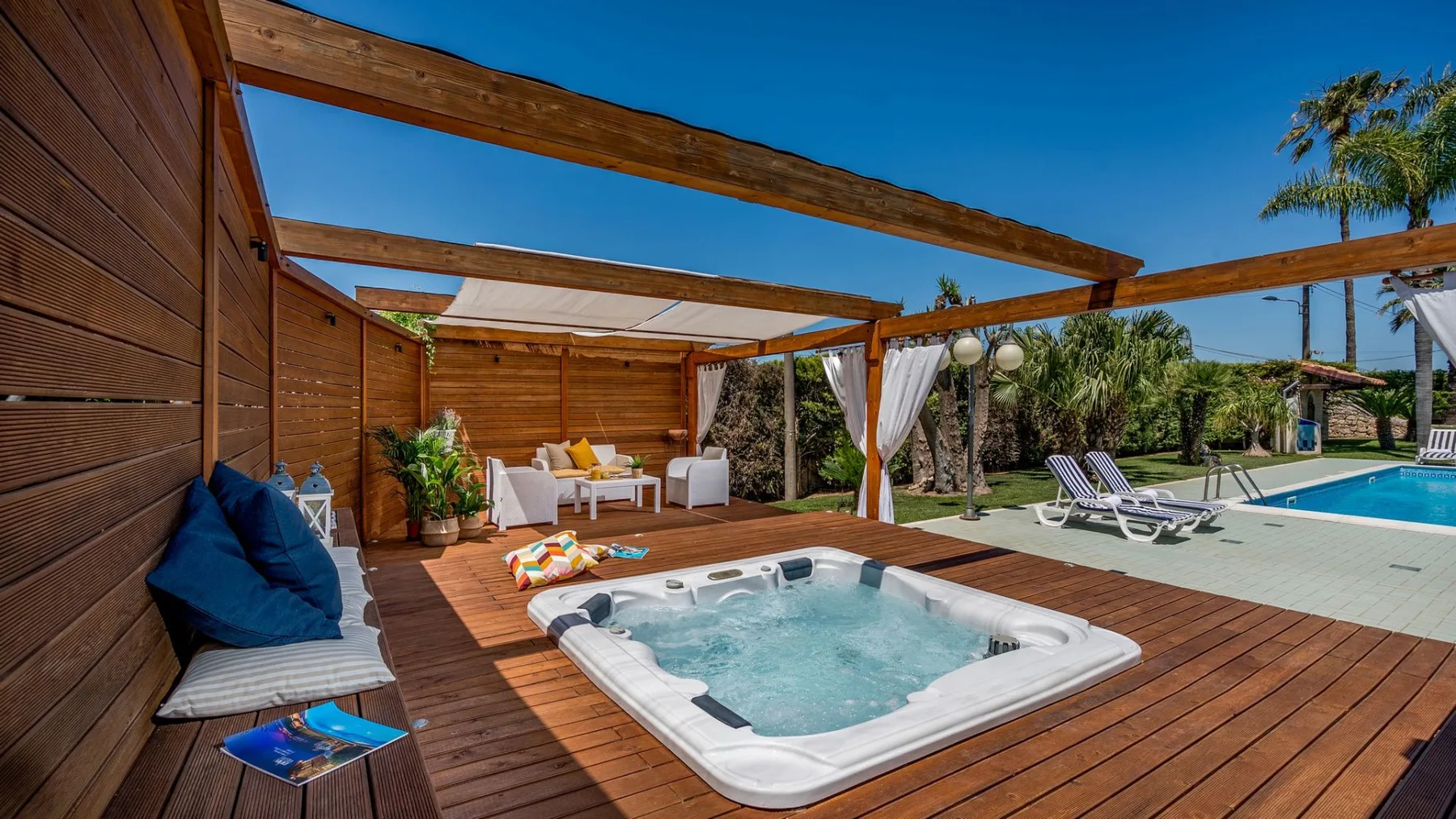 Una terraza de madera con una bañera de hidromasaje y una piscina junto a asientos al aire libre.