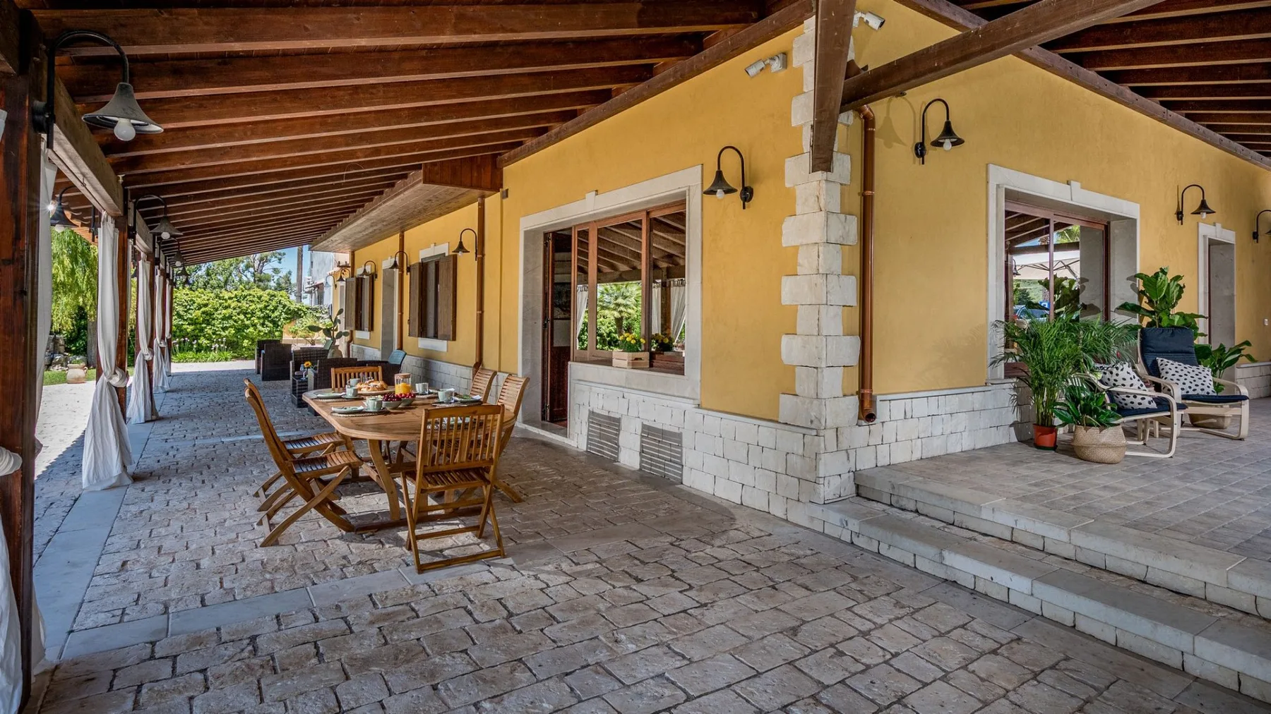 Una zona cubierta de comedor al aire libre se extiende junto a un edificio amarillo.