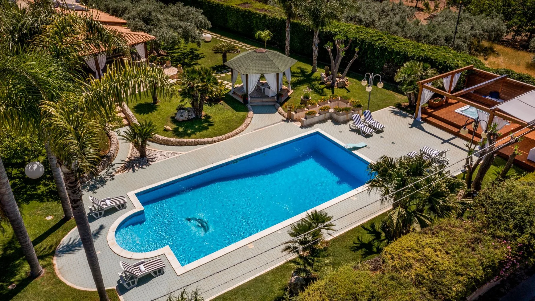 Una zona de piscina al aire libre ajardinada, con una pequeña glorieta y asientos alrededor.