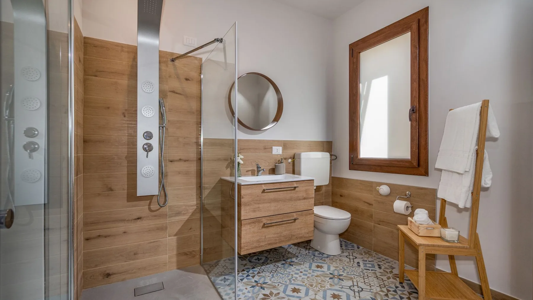 Un baño con ducha de vidrio, mueble de lavabo de madera y suelo de baldosas estampadas.