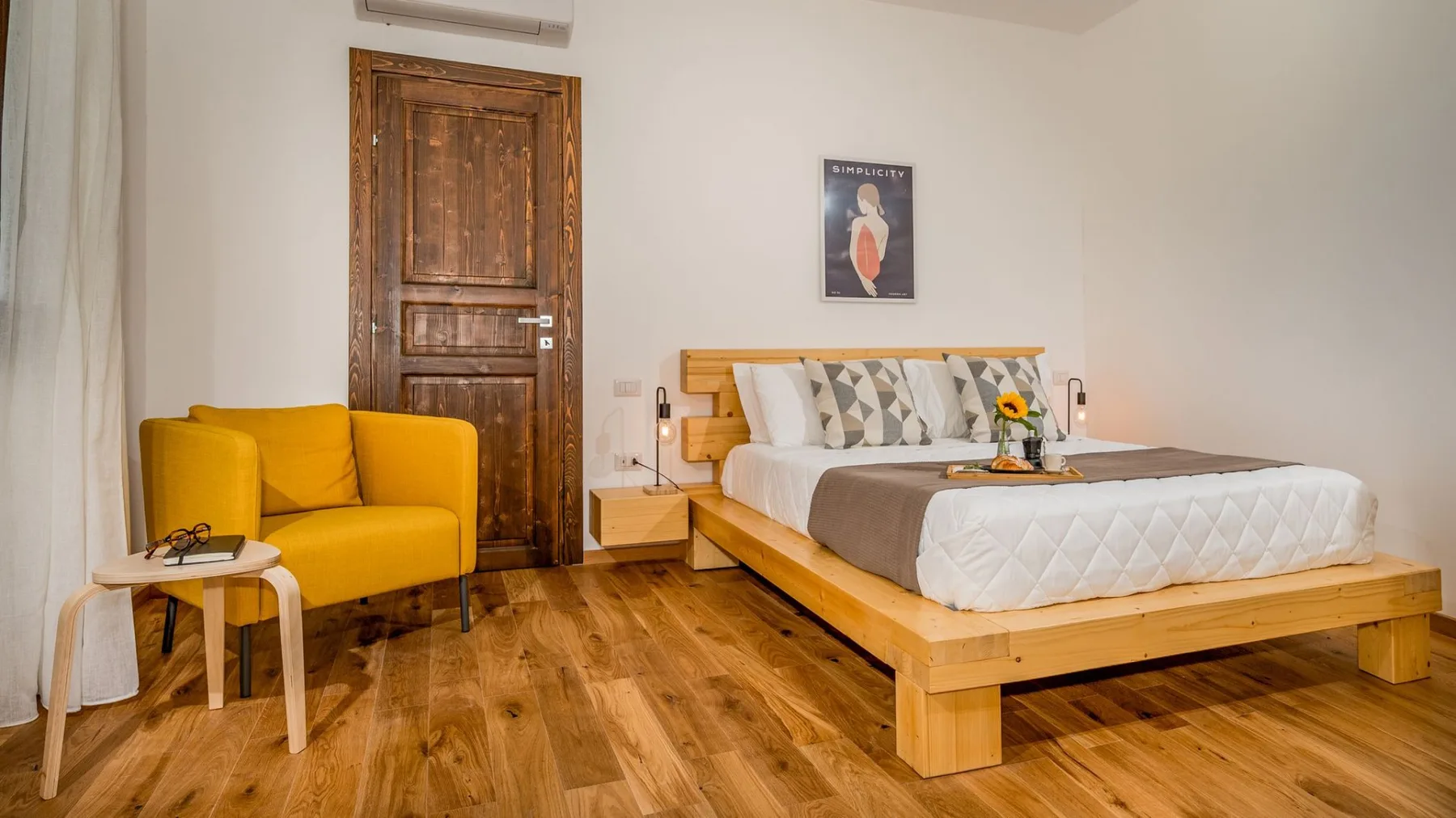Dormitorio con una cama de madera, ropa de cama blanca y un sillón amarillo mostaza.