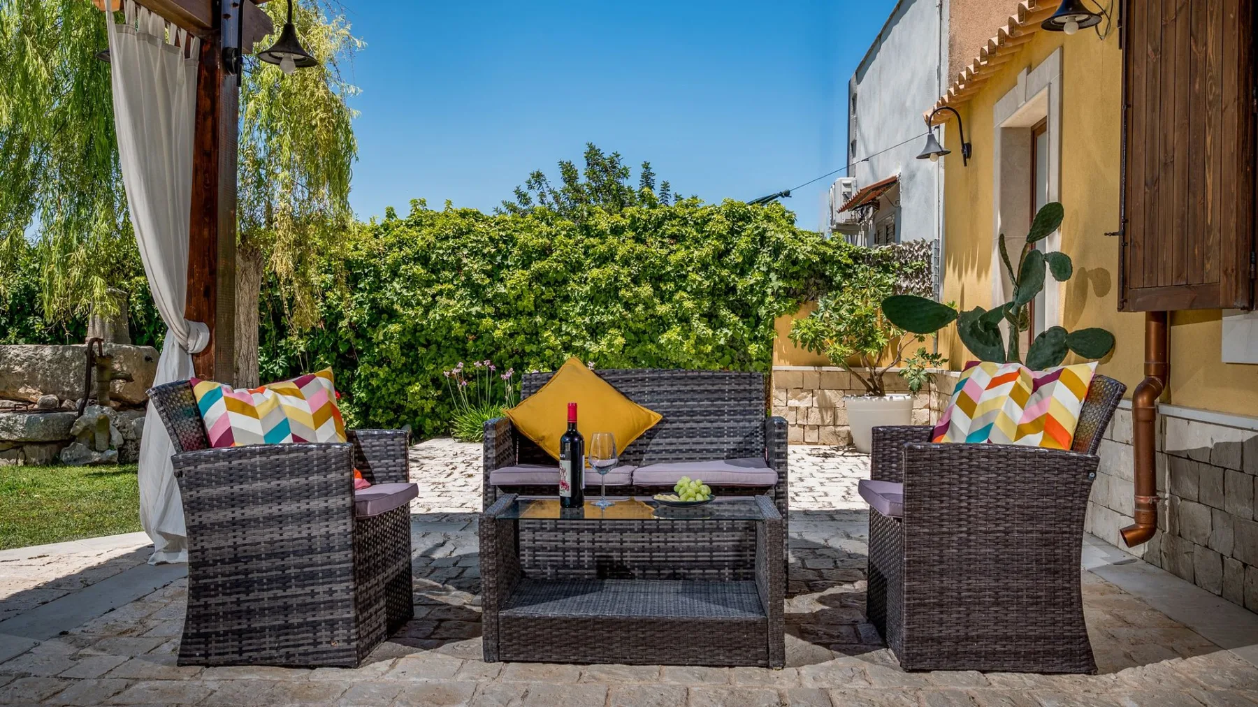 Un patio soleado al aire libre con asientos de mimbre alrededor de una mesa baja.