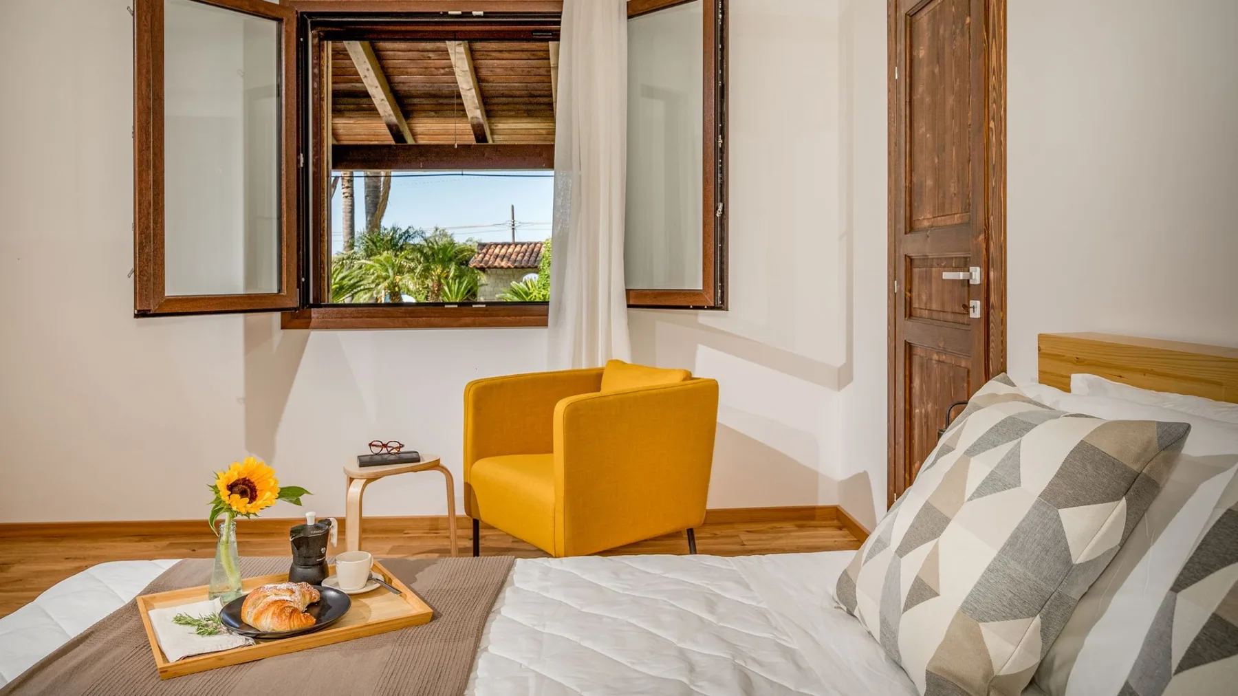 Dormitorio con una cama, asientos color mostaza y una ventana abierta.