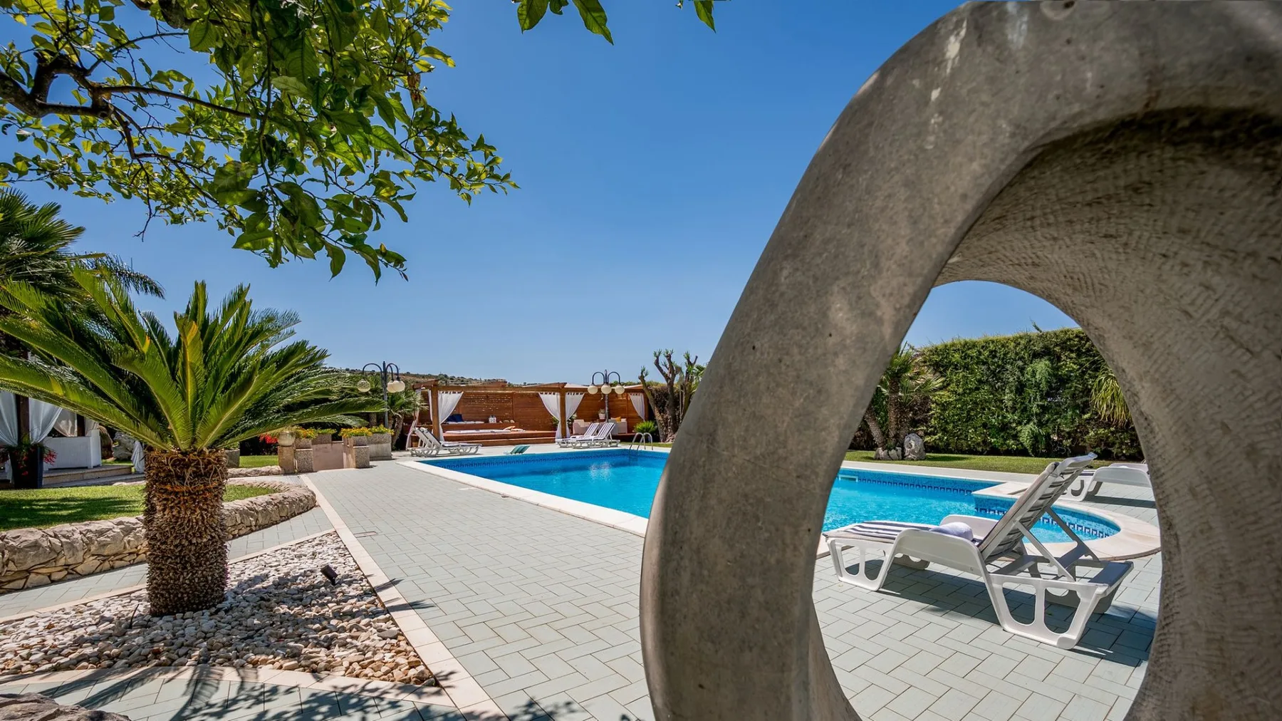 Una piscina al aire libre con tumbonas junto a un patio pavimentado.