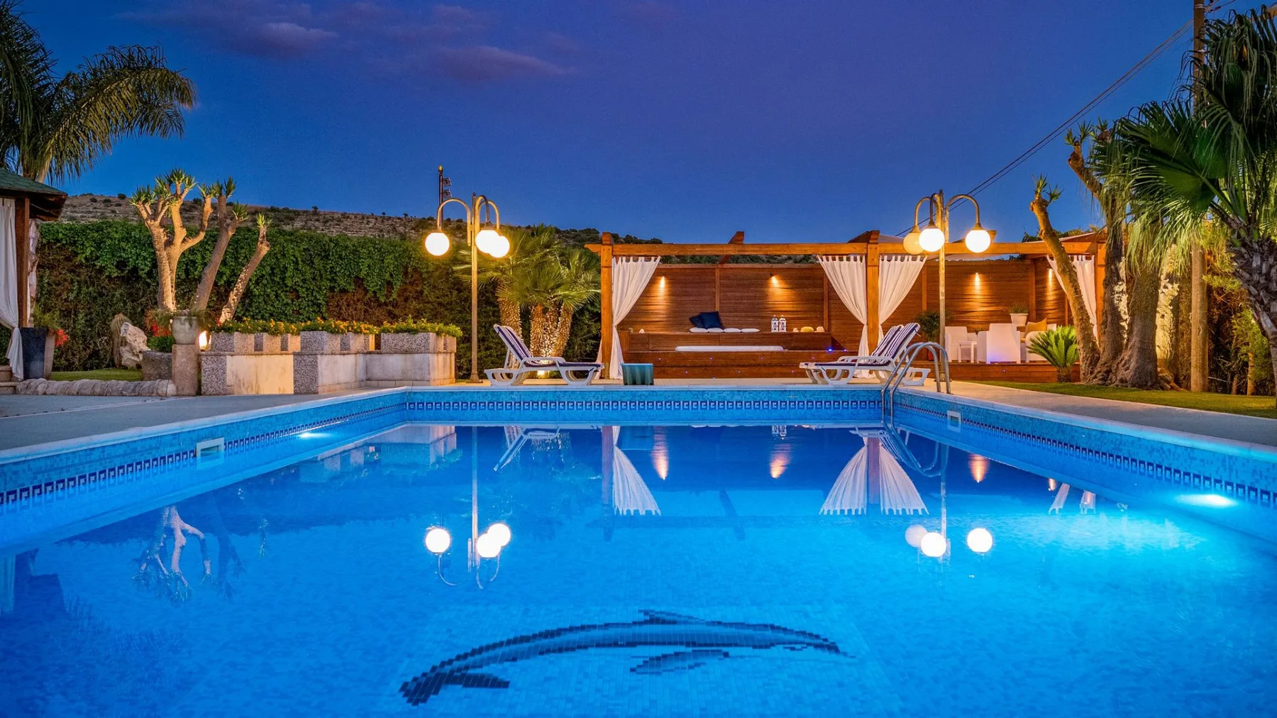 Una piscina exterior refleja las luces del atardecer junto a una zona de estar cubierta.