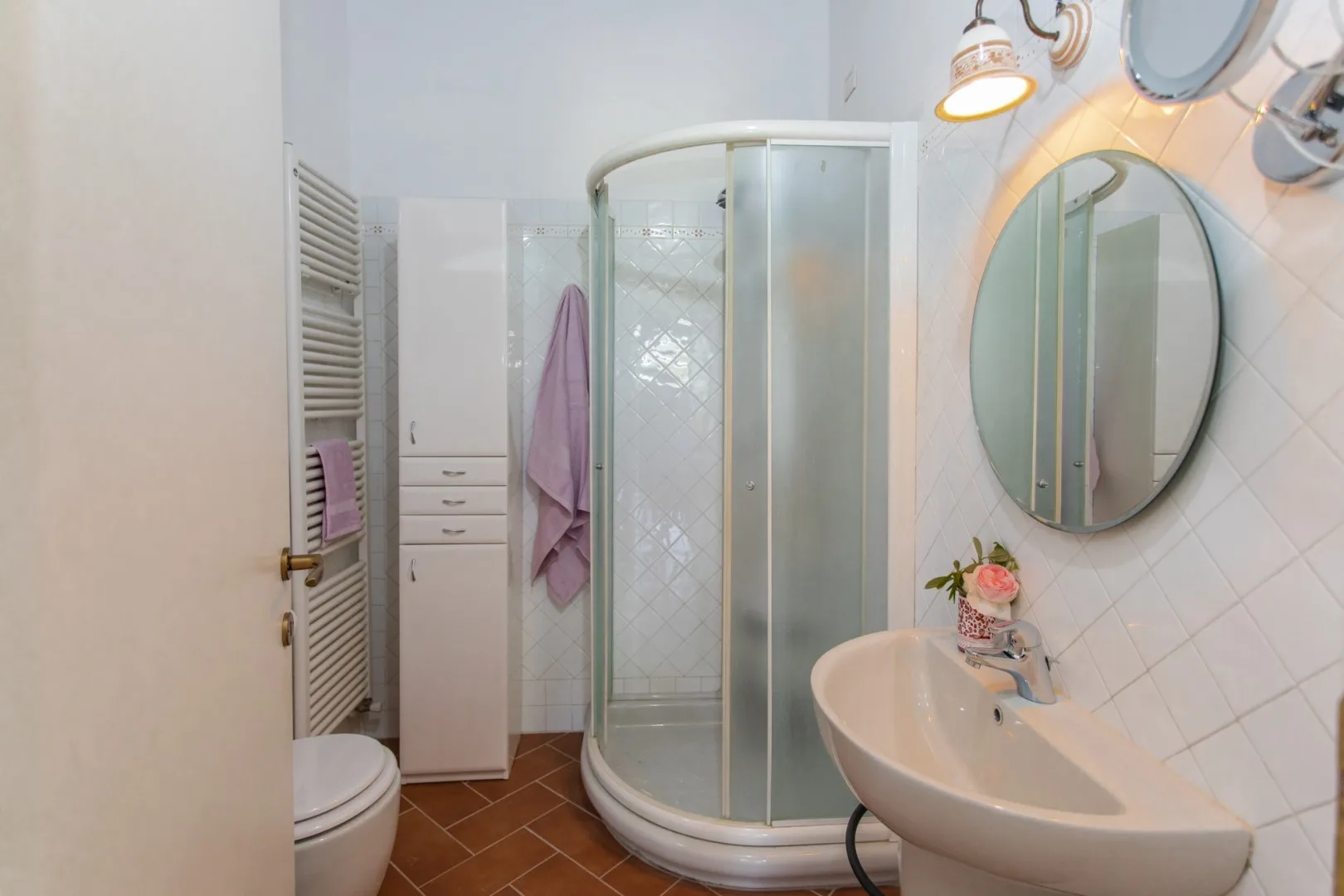 A bathroom with a curved glass shower, sink, and wall mirror.
