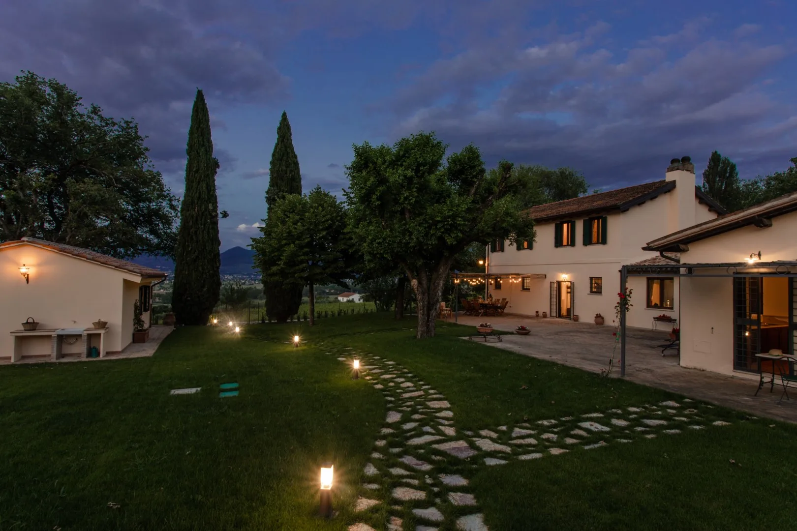 A landscaped courtyard path leads between white buildings under evening lights.