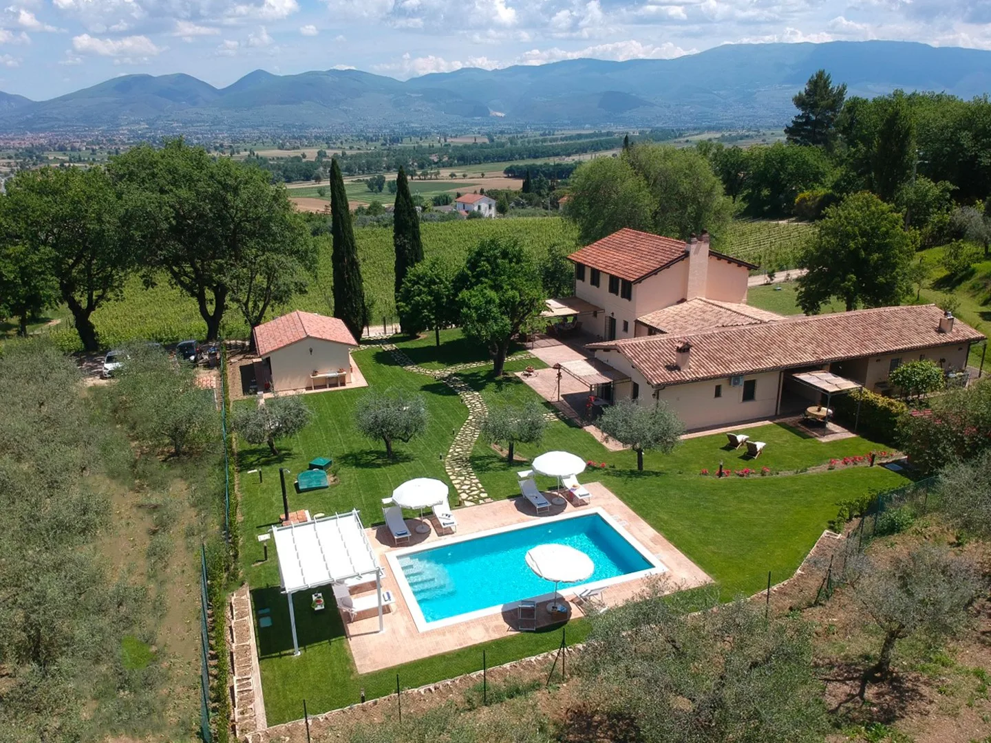 A countryside property with a swimming pool and landscaped grounds, set against distant hills.