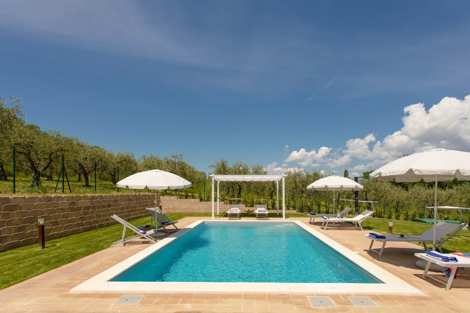An outdoor swimming pool surrounded by sun loungers and umbrellas.