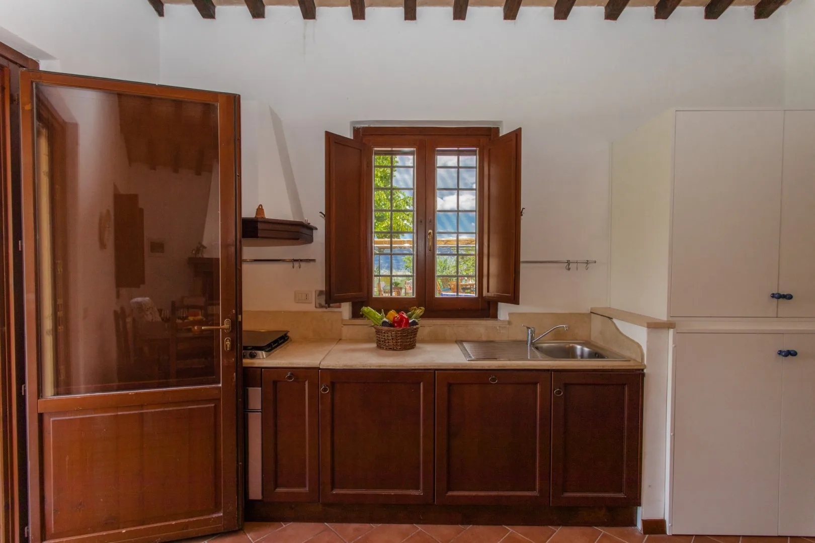 A kitchen with wooden cabinets, a sink, and a window overlooking greenery.