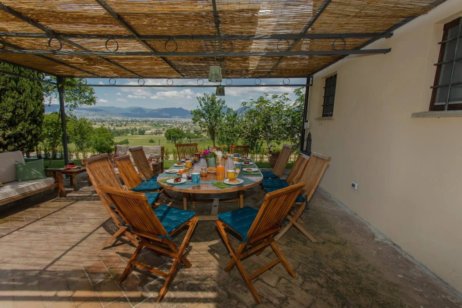 A covered outdoor dining area with a table and seating overlooking a green valley.