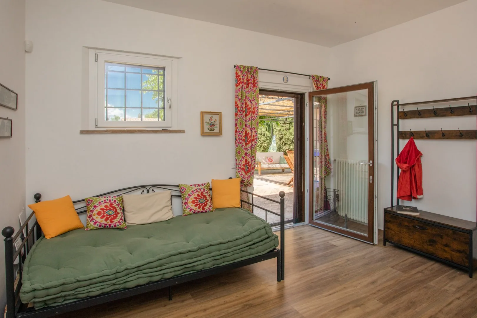 A bedroom with a green daybed and an open glass door leading outside.