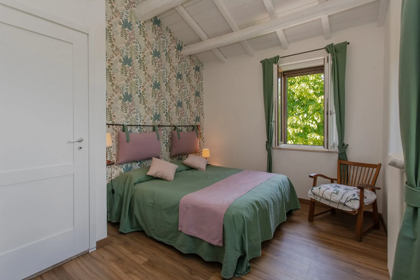 A bedroom with a green-covered bed beside a window overlooking leafy trees.