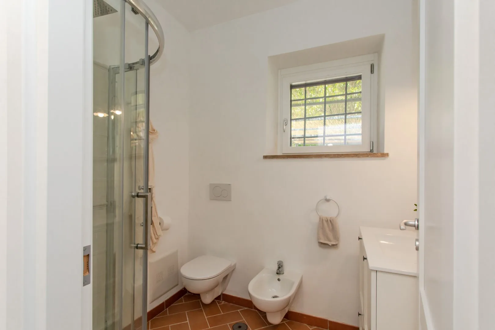 A compact bathroom with a glass shower, toilet, and small window.