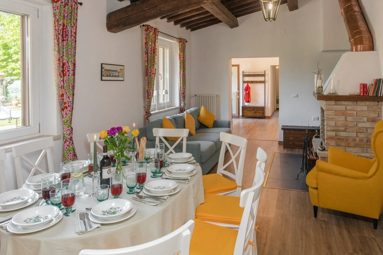 A dining area with a set table, seating, and a living space beside a brick fireplace.