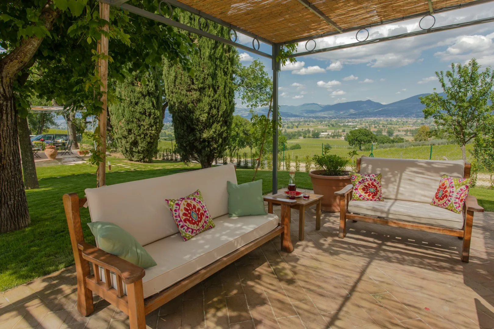 A shaded outdoor seating area overlooks a green valley and distant mountains.
