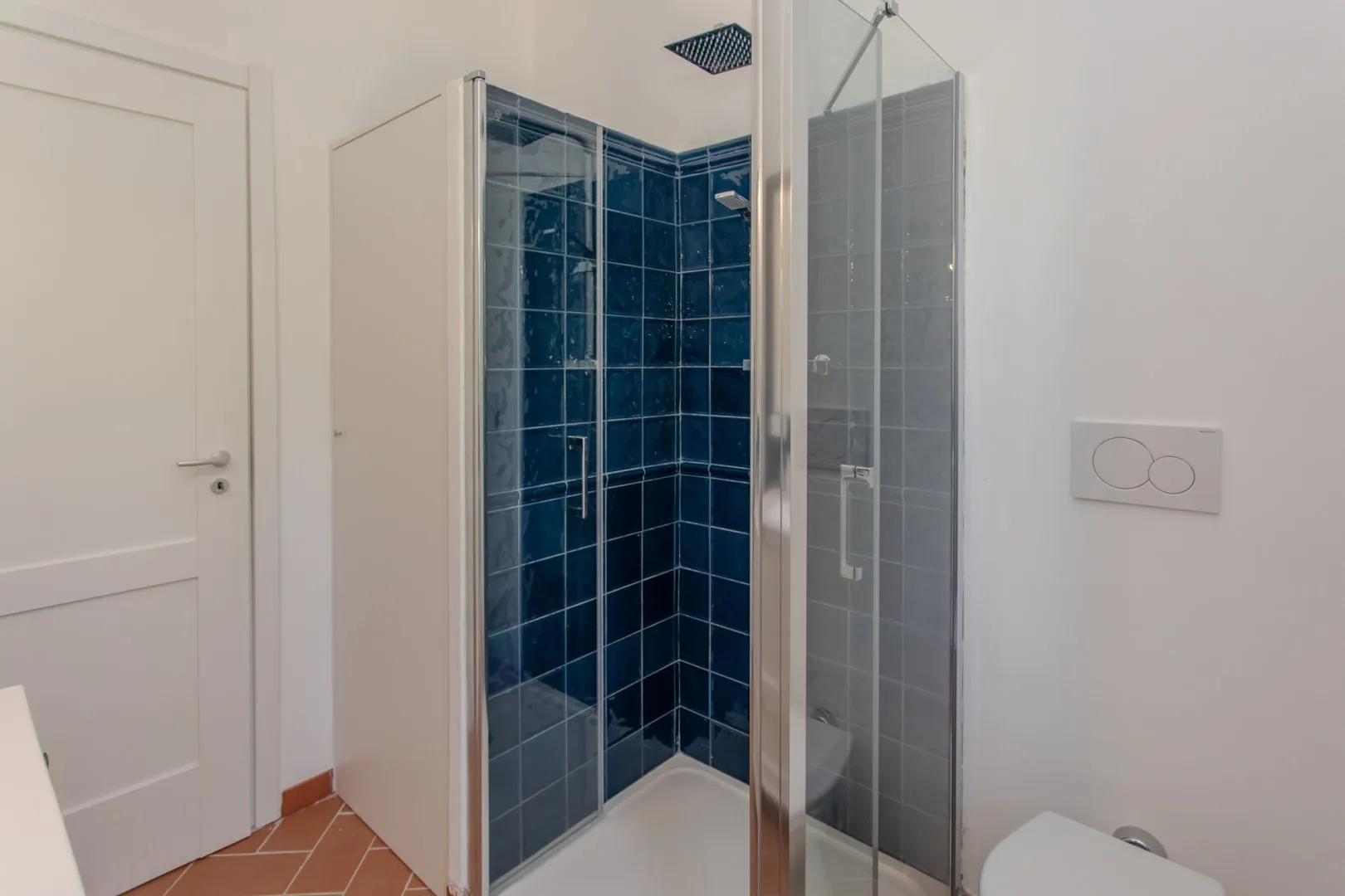 A bathroom with a glass shower and dark blue tile.