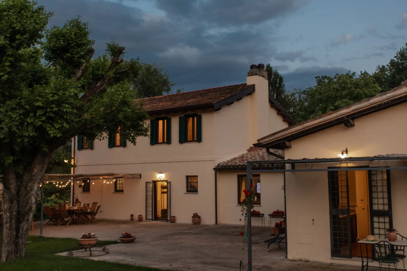 A pale two-story building faces a paved courtyard beneath a cloudy evening sky.