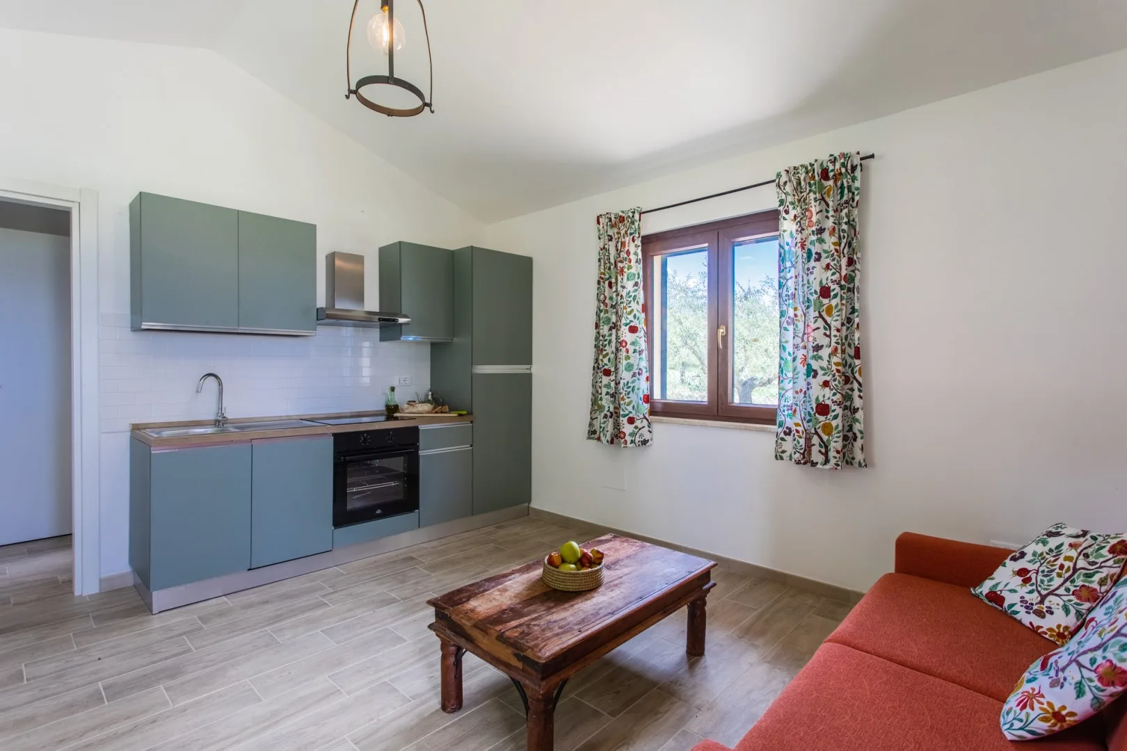 A living area with a compact kitchen, a wooden coffee table, and a red sofa.