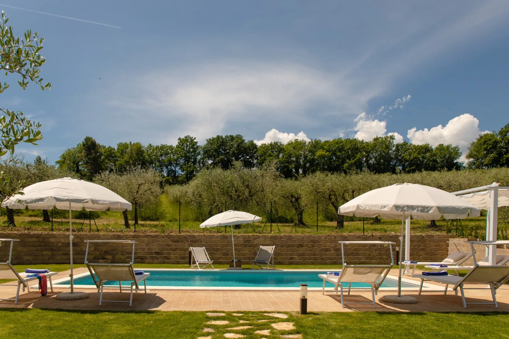 An outdoor swimming pool is surrounded by lounge seating and sun umbrellas.