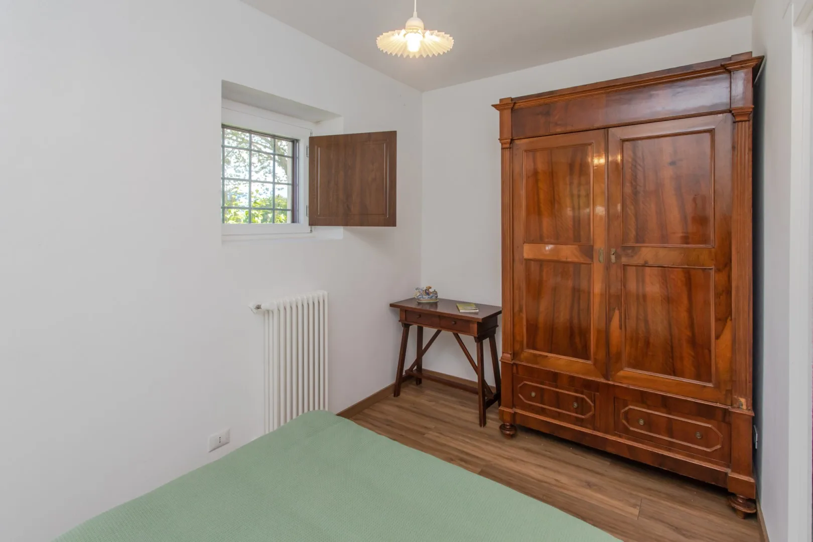 A bedroom with a wooden wardrobe, a small table, and a window.