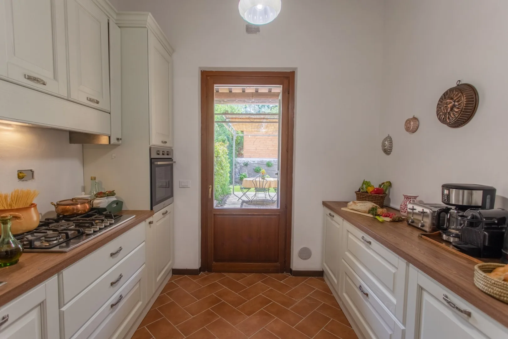 A narrow kitchen with white cabinets, wooden counters, and a glass-paneled door.