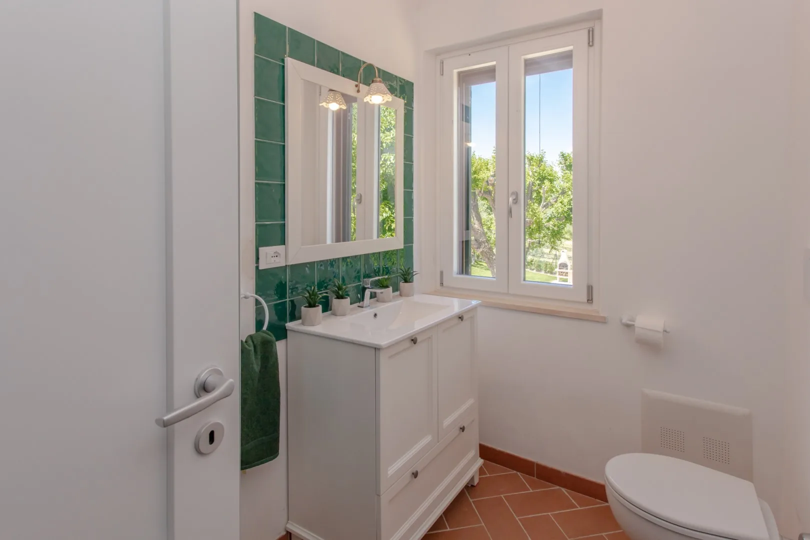 A bright bathroom with a sink vanity, green tile, and a window.