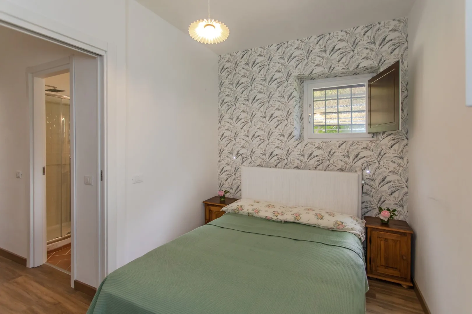 A bedroom with a green bedspread, patterned wallpaper, and a small window.