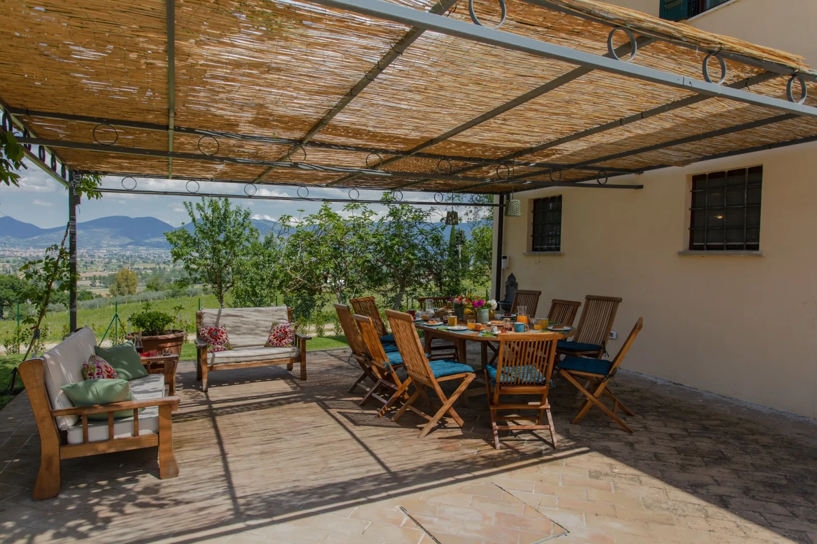 A shaded outdoor dining area with a long table and surrounding seating.