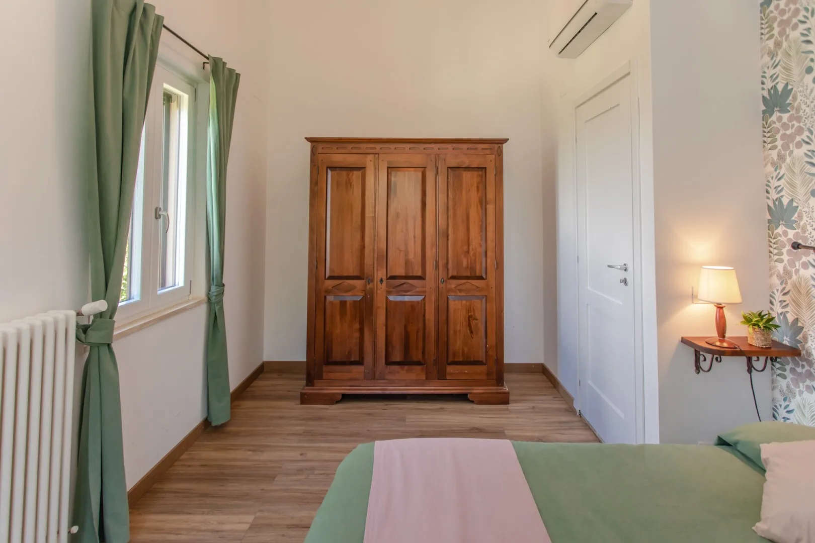 A bedroom with a wooden wardrobe, a window, and a bed.