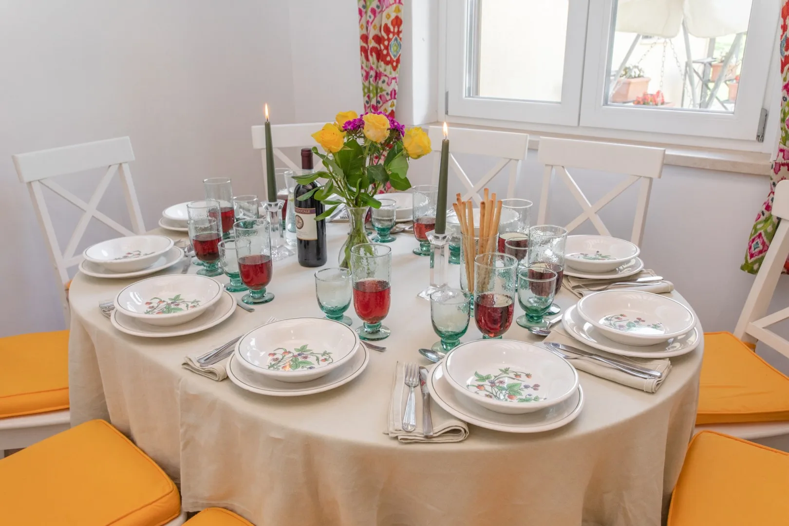 A dining area with a round table set with plates, glasses, and flowers.