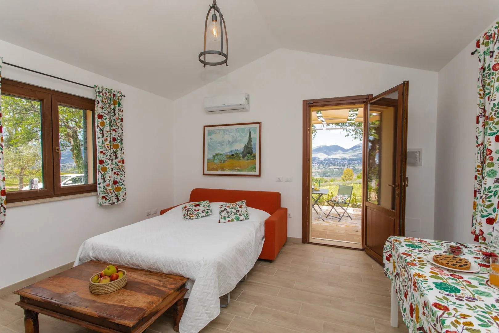 A bright bedroom with a bed, orange seating, and an open door to a balcony.