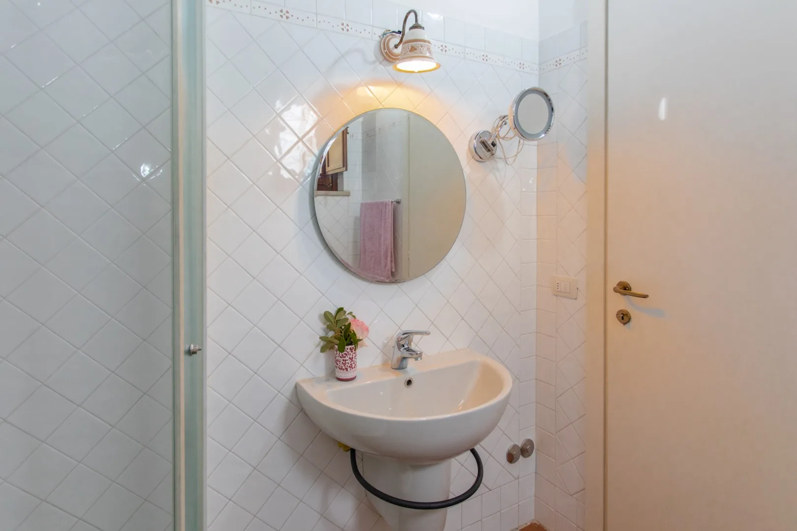 A tiled bathroom with a wall-mounted sink and round mirror.