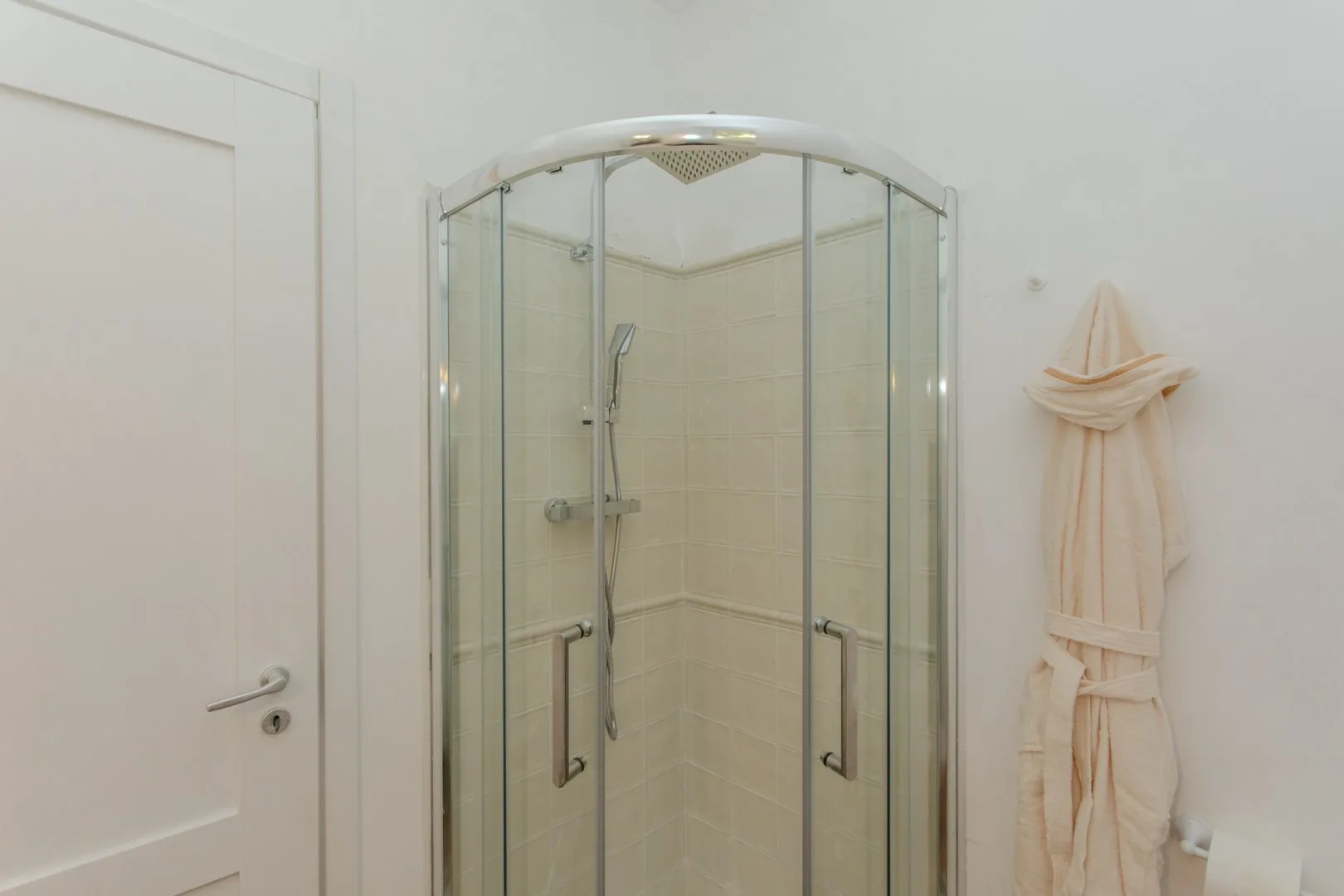 A tiled bathroom with a glass-enclosed shower and a hanging robe.