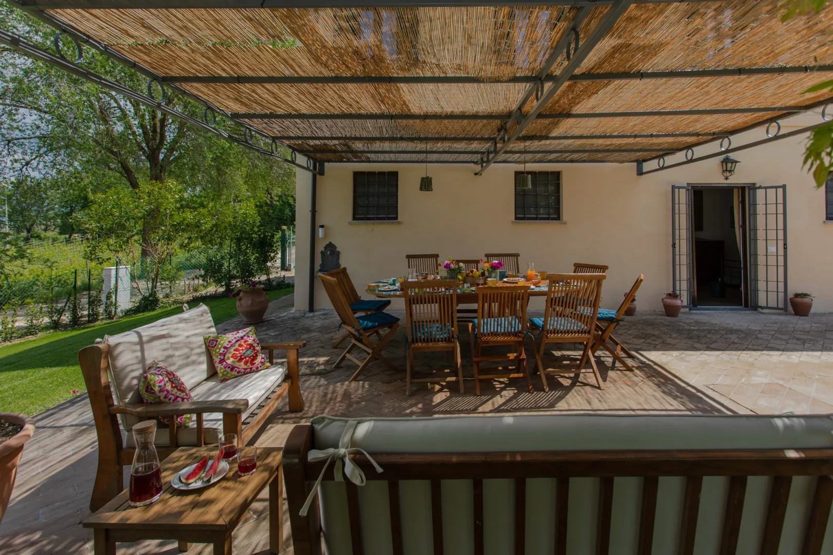 A shaded outdoor dining area with a wooden table and seating.